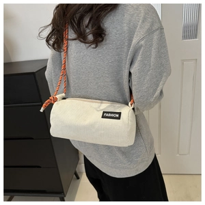 Detail of cream corduroy cylinder bag with orange woven rope strap and fashion label
