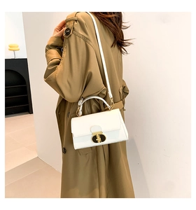 Dettaglio borsa a mano bianca in pelle con chiusura dorata indossata su trench kaki