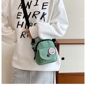 Close-up of green canvas crossbody bag with cute bunny badge and adjustable strap