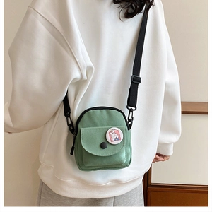Detail view of mini green canvas crossbody bag with cartoon badge and black nylon strap