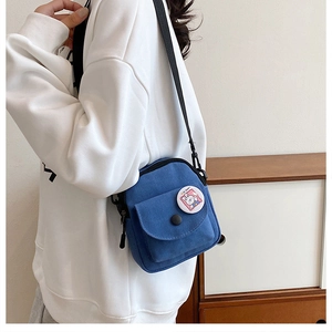 Blue canvas crossbody bag with cute badge and adjustable strap worn by a model