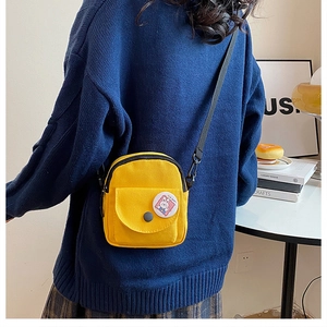 Mini yellow canvas crossbody bag with cartoon bunny badge worn over a navy sweater