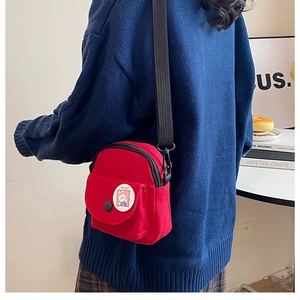 Close-up of a mini red canvas crossbody bag with a cute rabbit badge and adjustable strap