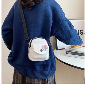 Close-up of mini white canvas crossbody bag with adjustable strap and cute rabbit brooch