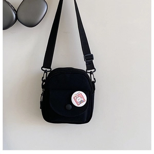 Detail of black mini canvas crossbody bag with magnetic front pocket and cartoon badge