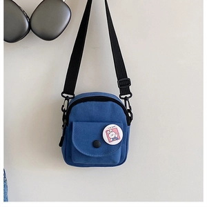 Detail of blue canvas mini crossbody phone bag with adjustable strap and cartoon badge