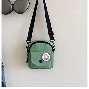 Detail of light green canvas crossbody bag featuring adjustable black strap and cute badge
