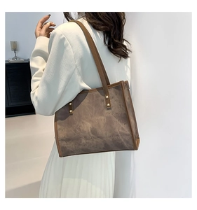 Side view of a vintage brown tote bag with gold studs worn over a white suit