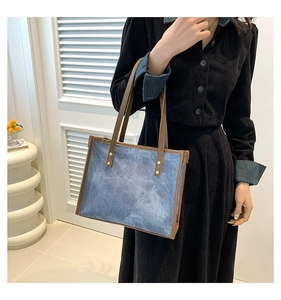 Detail of vintage tote bag featuring blue textured fabric and brown leather handles