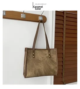 Close-up of caramel canvas tote bag with leather trim and metal rivets hanging on a hook