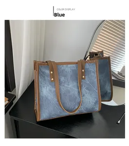 Detail of blue denim tote bag with brown leather handles and golden rivets on black wood