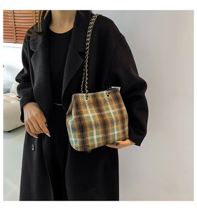 Detail of wool plaid bucket bag with gold chain strap on black coat background