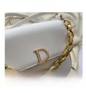 Détail du sac selle en cuir blanc avec grosse chaîne dorée et boucle en métal en forme de D