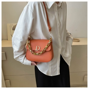 Détail d'un sac besace orange avec chaîne dorée et boucle métallique sur un mannequin
