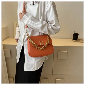 Détail d'un sac selle orange vif avec boucle en D dorée et bandoulière en chaîne