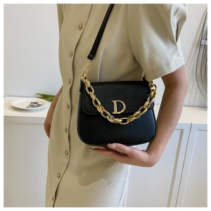 Détail du sac selle en cuir noir avec chaîne dorée et logo D porté par le mannequin
