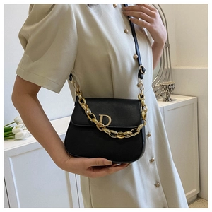 Détail du sac selle en cuir noir avec boucle dorée en forme de D et bandoulière chaîne