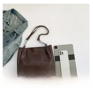 Detail of dark brown tote bag with crocodile pattern next to a tablet and jacket