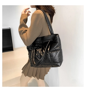 Detail of a black quilted puffer tote bag with glossy finish on a shoulder model
