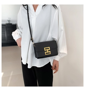 Detail of a black leather crossbody bag featuring a classic gold square buckle closure