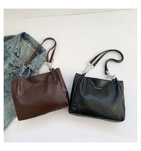 Detail of crocodile-textured tote bags with silver chain handles in brown and black