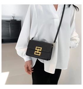 Detail of elegant gold geometric metal clasp on a stylish black crossbody flap bag