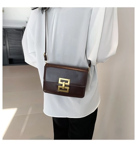 Detail of dark brown leather crossbody bag with a distinctive gold square metal buckle
