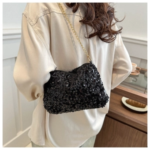 Model view of black sequin evening bag with gold chain strap in a cozy interior setting