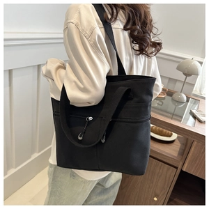 Détail du sac cabas en toile noire montrant la poche zippée et la large bandoulière