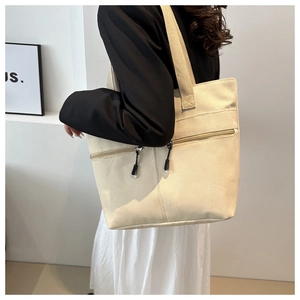 Détail du sac cabas en toile crème montrant la large bandoulière et les poches zippées
