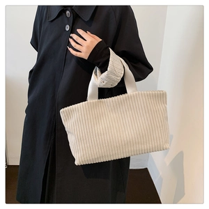 Detailed shot of cream corduroy tote bag styled with a black coat for fall fashion