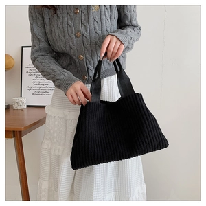 Close-up of black corduroy tote bag featuring vertical ribbed texture and reinforced handles