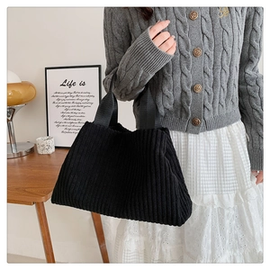Detail of black corduroy tote bag showing textured vertical ribs and wide nylon handle