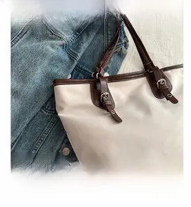 Detail of canvas tote bag showing brown leather trim and metal buckle accents
