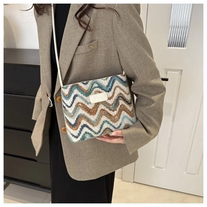 Detail of wool bucket bag featuring wavy knit texture and logo patch with crossbody strap