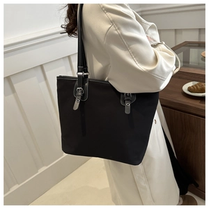 Detail of a large black tote bag with leather straps and silver buckles shown on a model