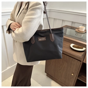 Black nylon tote bag with brown leather handles worn by a model in a cafe setting