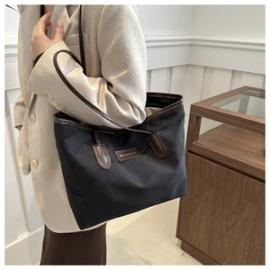 Detail of black nylon tote bag with leather straps on model in cream setting
