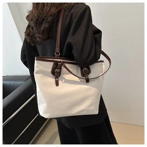 Close-up of a large canvas tote bag with brown leather trim worn by a model