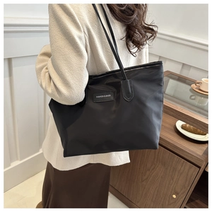 Detail of a large black nylon tote bag with a fashion square label and leather straps