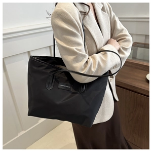Model wearing a large black nylon tote bag with leather straps and fashion label