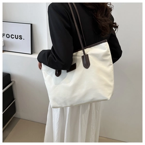 Detail of a large white nylon tote bag with contrast brown leather handles for commuting