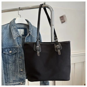 Close-up of black canvas tote bag with adjustable silver buckles on stainless steel hanger