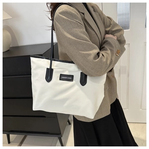 Chic cream nylon tote bag with black straps worn by model in a modern room setting