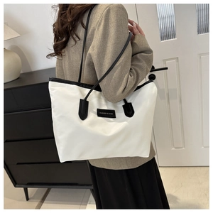 White nylon tote bag with black leather straps and fashion label in a home setting