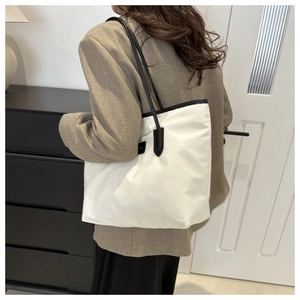 Detail of white nylon tote bag with black leather trim and slim shoulder straps on model