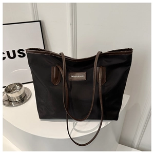 Detail of black nylon tote bag with brown leather handles and fashion logo patch
