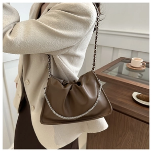 Détail d'un sac froncé marron foncé avec chaîne dorée sur un blazer beige chic
