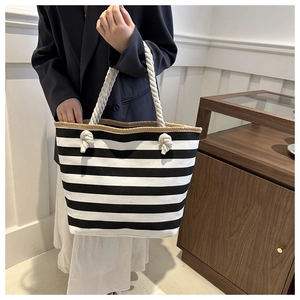 Detail of striped canvas tote bag featuring thick rope handles and woven straw edge trim