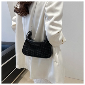 Detail of black rhinestone crescent hobo bag with metal chain strap on model in white suit